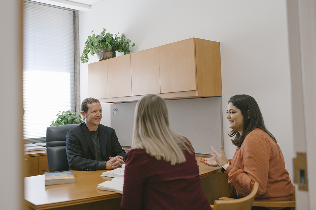 two GWSB students chat with a professor in his office