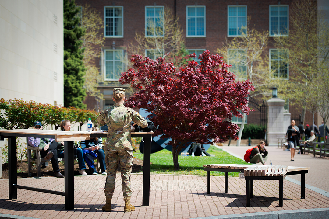 a student in military fatigues stands in Kogan Plaza on the GW campus