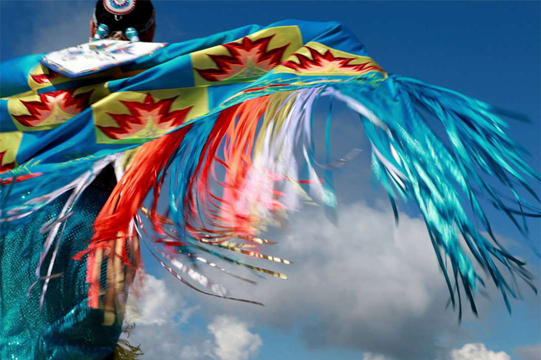 a Native American in colorful clothing dances during a tribal event