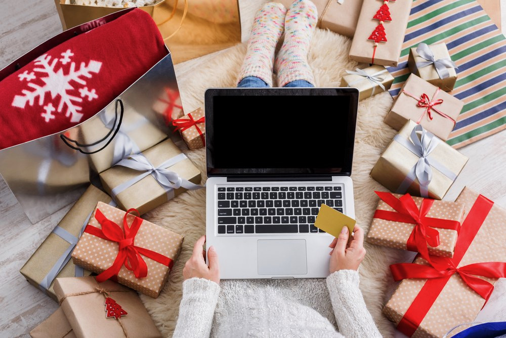 image shows a person with a laptop eating a cookie while surrounded by Christmas presents