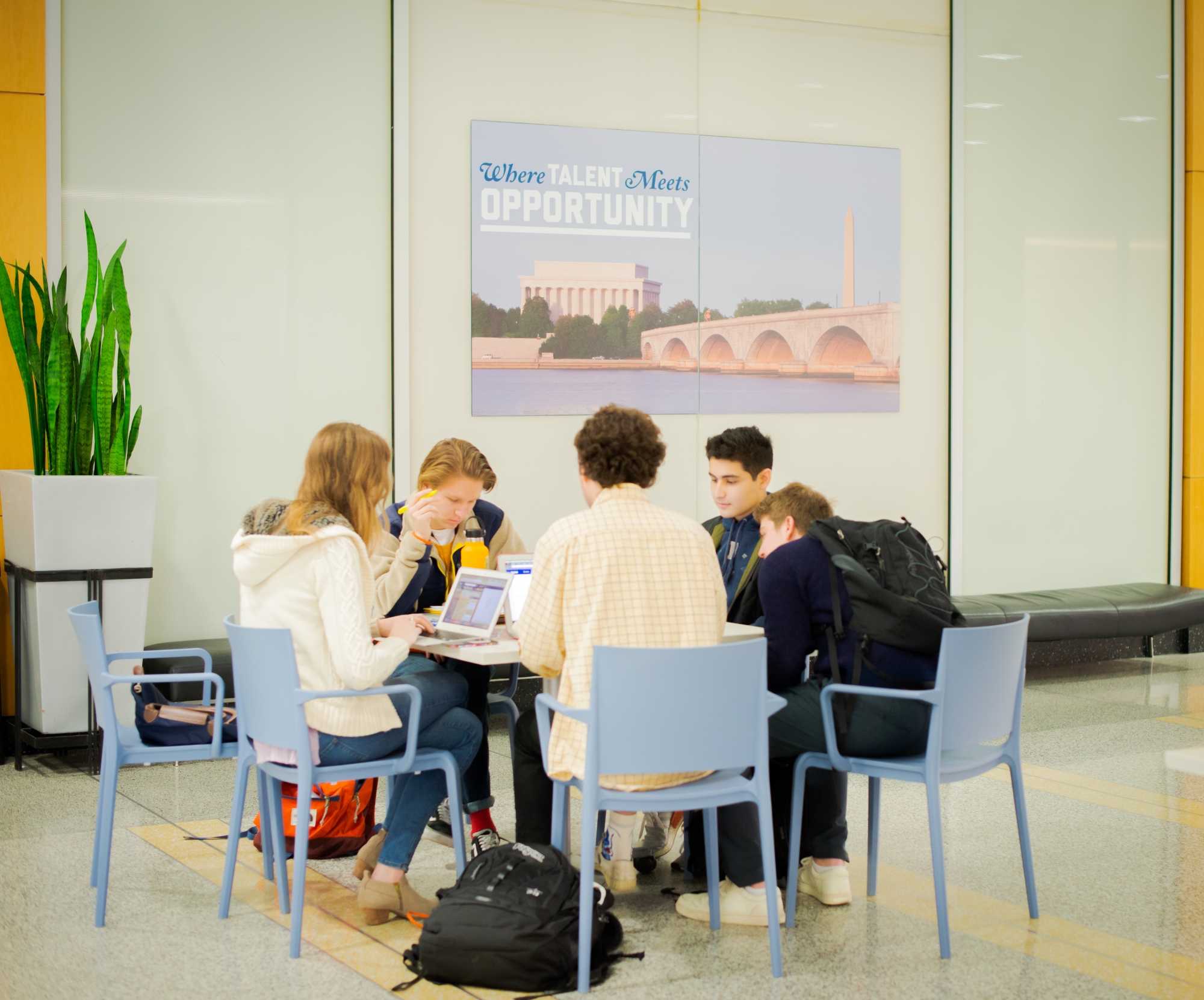 Five students seated around a table, poster in background reads "Where talent meetings opportunity"