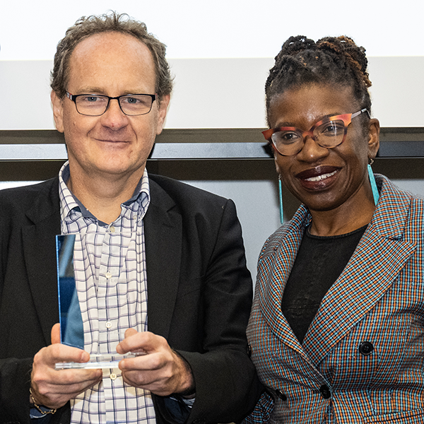 two people stand side by side smiling one on left holding reward