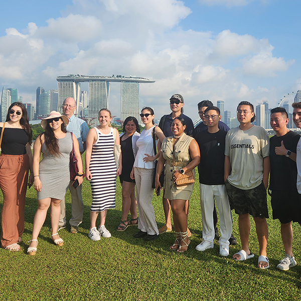 Students in GW's global bachelors program post for a photo on a grassy lawn in Singapore the city skyline with the iconic Marina Bay San hotel is visible in the distance behind them