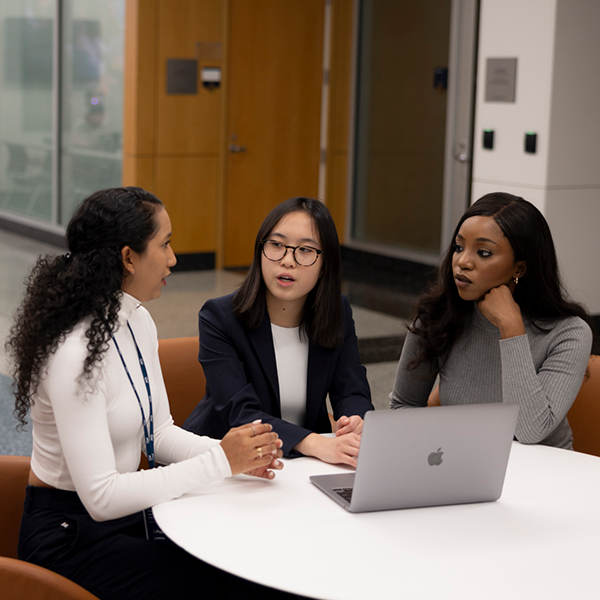 Thee people sitting at a table in front of laptop having discussion